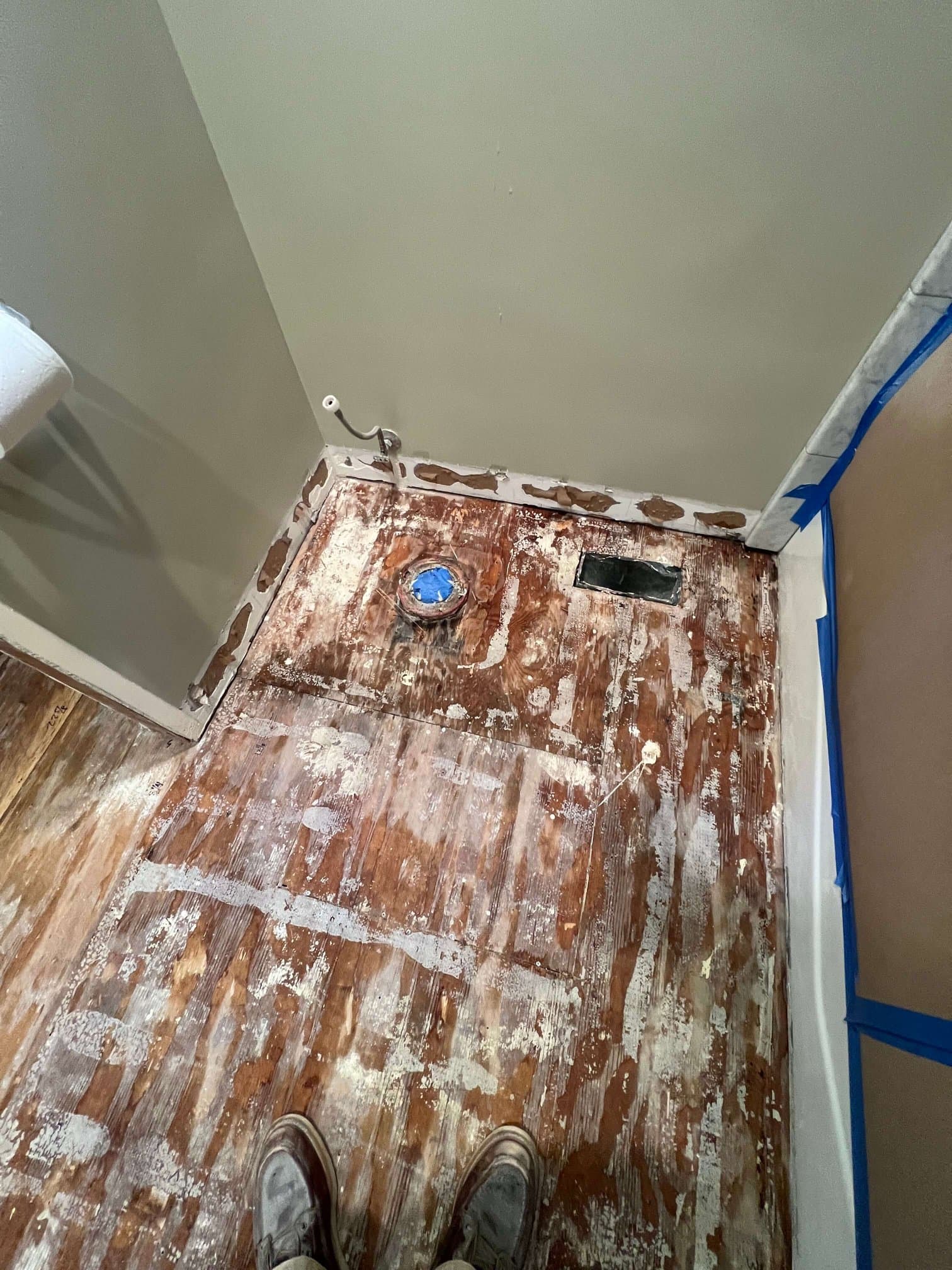 Bathroom subfloor exposed down to the original wood, with a toilet flange taped off before tile