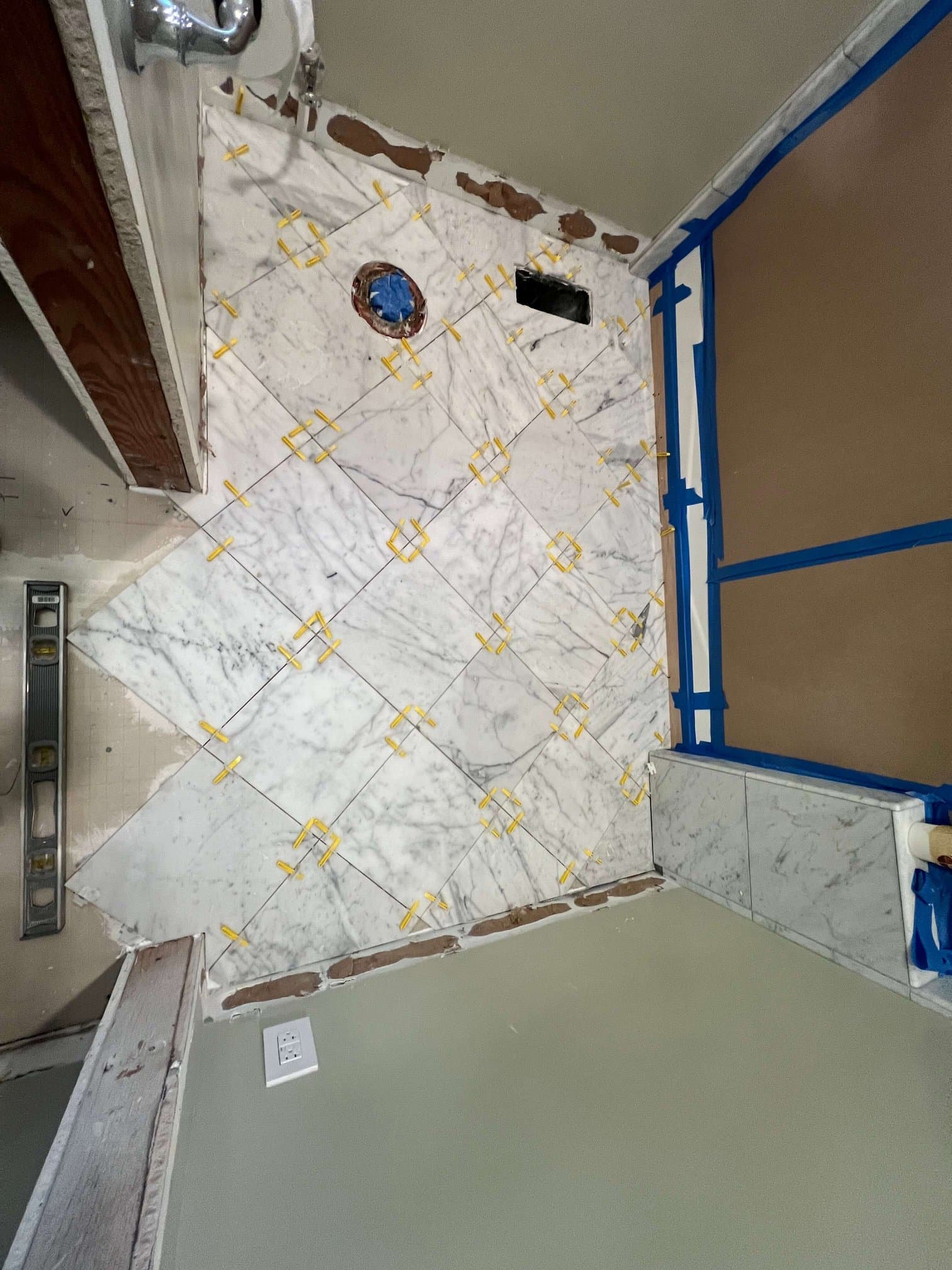 White marble floor tile being set on the diagonal with yellow spacers in a bathroom