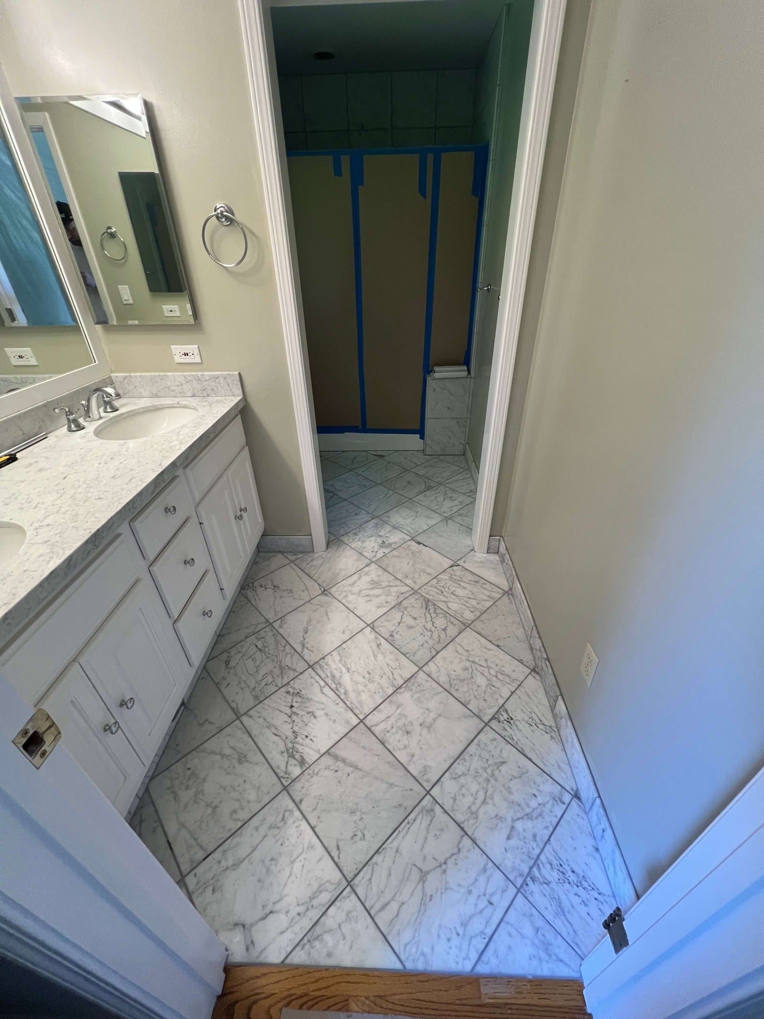 Finished diagonal marble tile floor in a bathroom with a white vanity and marble counter