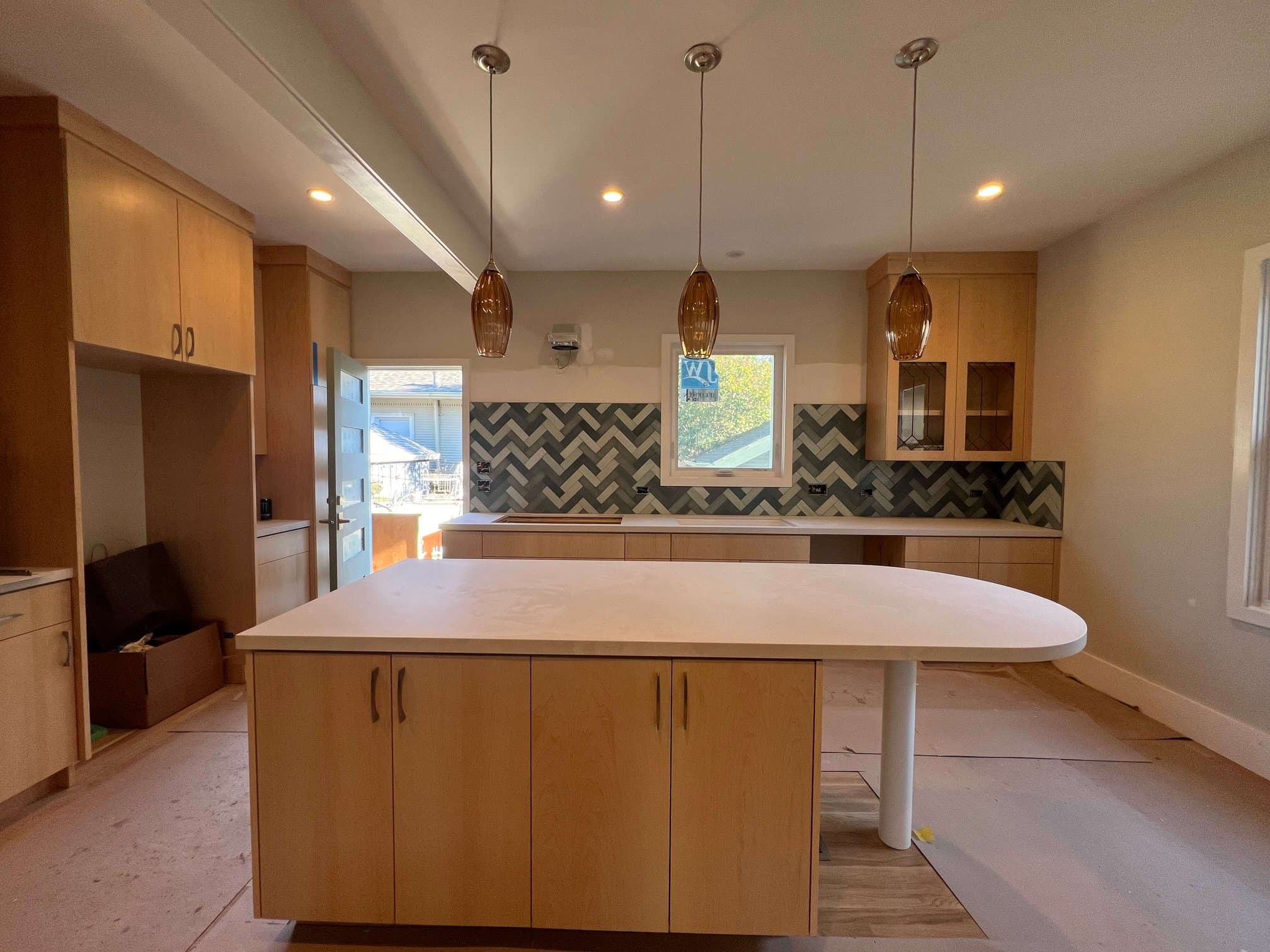 Kitchen remodel with a maple island, light counters, herringbone tile backsplash, and pendant lights