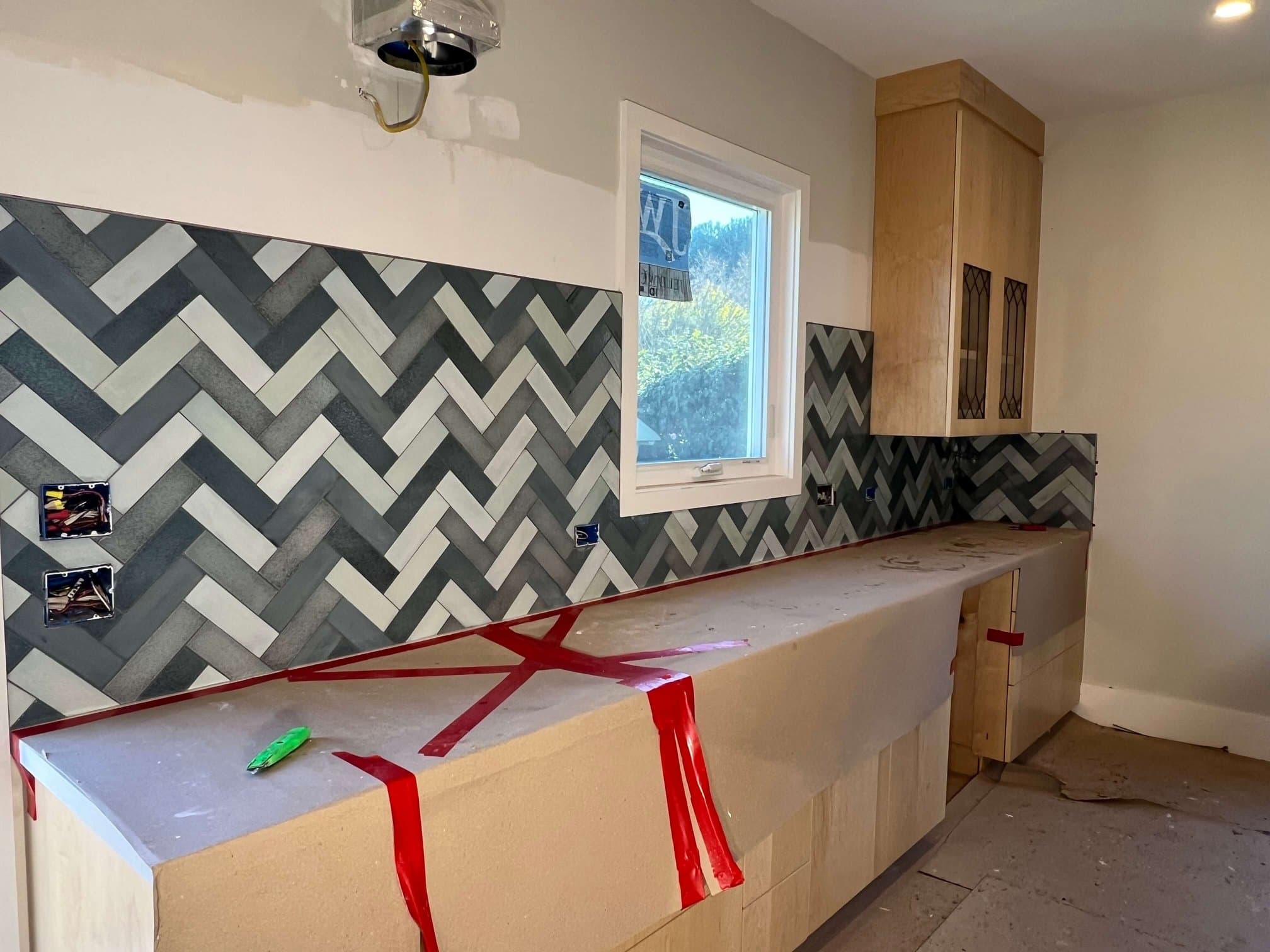 Gray and white herringbone tile backsplash along a kitchen run, with the counters still protected