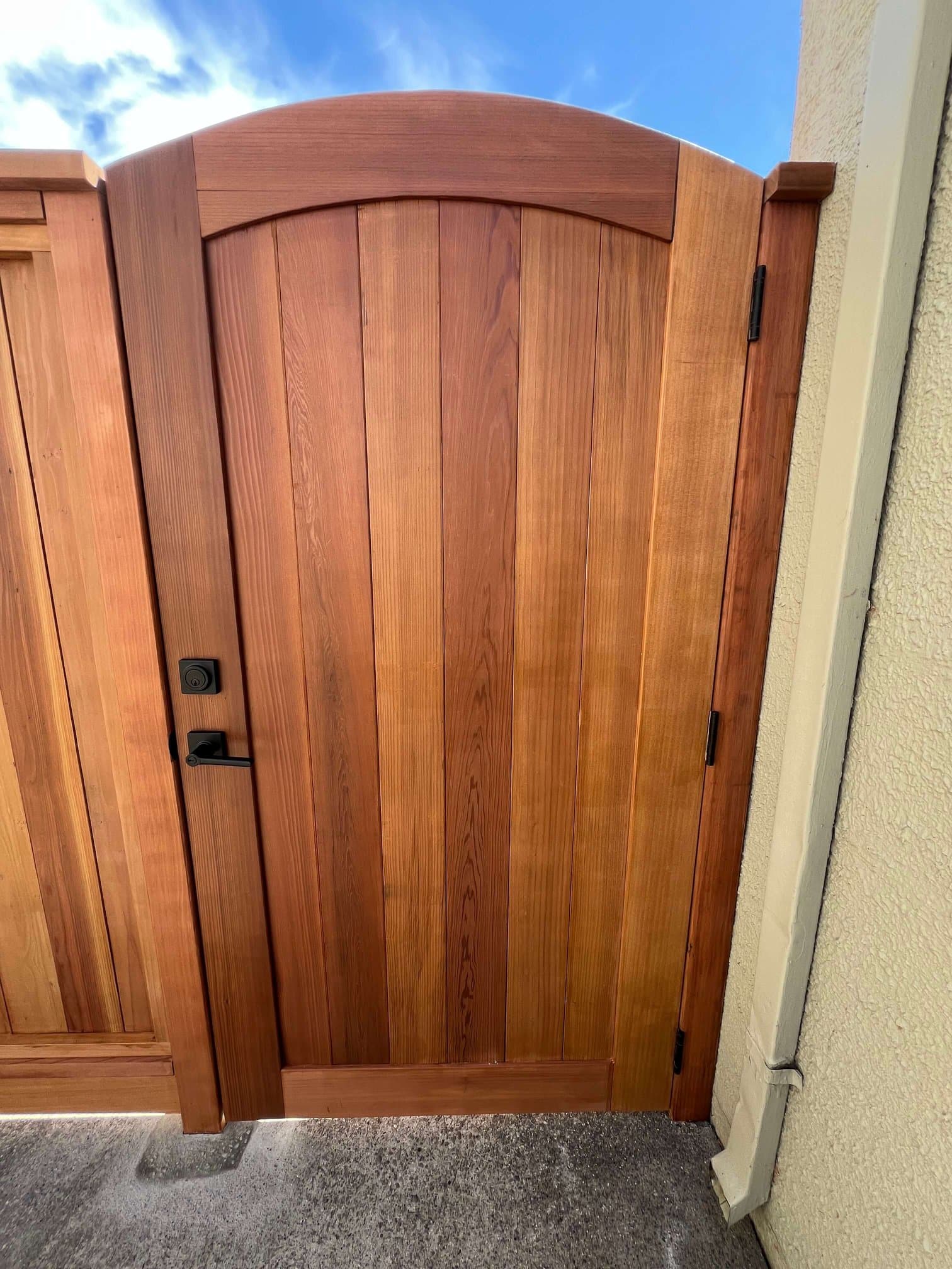 Close-up of a custom arched cedar gate with black latch and keypad