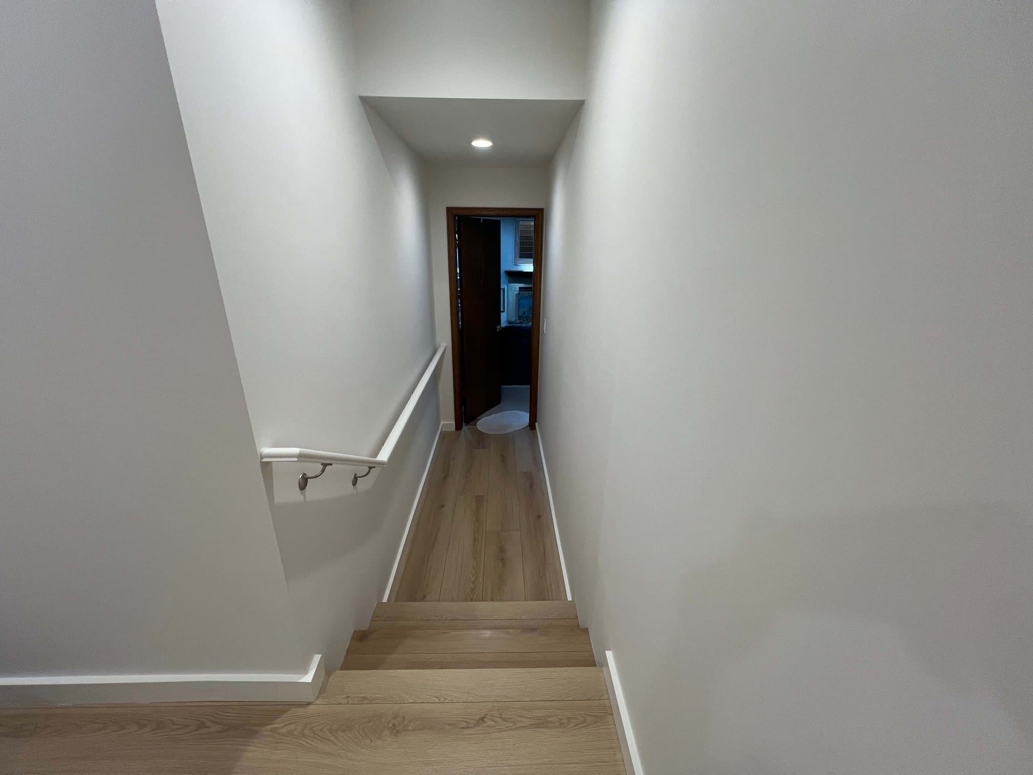 Matching light oak laminate on a stair run and hallway with a white wall-mounted handrail