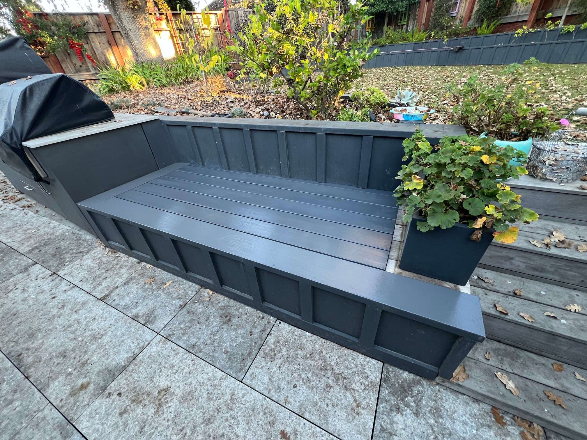 Custom charcoal-gray backyard bench built into an outdoor kitchen beside a BBQ