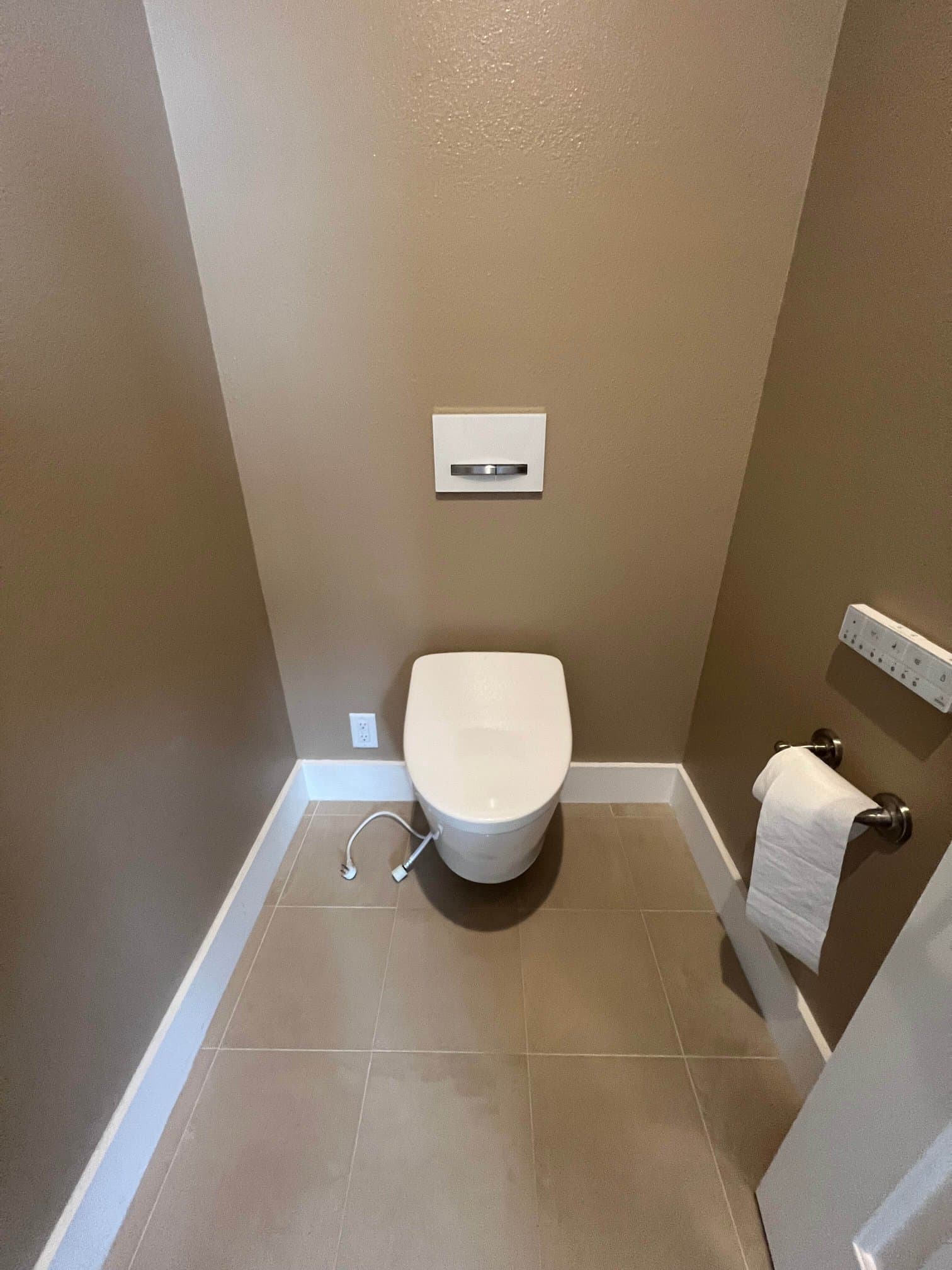 Finished wall-hung toilet with in-wall flush plate and beige tile floor